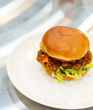 A golden-fried chicken sandwich topped with melted cheese, fresh lettuce, and pickles on a toasted bun, plated professionally.