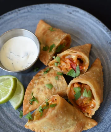 Golden-brown crispy spring rolls filled with vegetables, served with creamy dipping sauce and fresh lime garnish for food service.