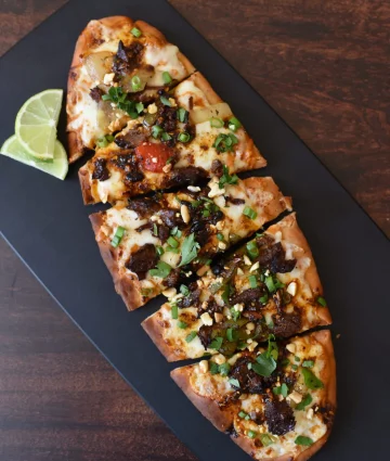 Plated seared salmon fillet topped with crispy garlic, green onions, and spicy garnish, served with lime wedge.